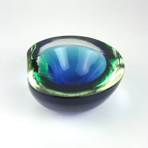 Könnte beinhalten: Eine kleine, abgerundete Glasschale mit einem tiefblauen Inneren, das in einen leuchtend grünen Rand übergeht. Die dicken, klaren Glaswände erzeugen einen geschichteten Farbeffekt, mit einer glatten, polierten Oberfläche und einer weiten, runden Öffnung.