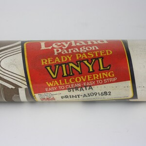 Op de afbeelding: Een rol bruin en wit vinyl behang met een golvend patroon. Het label vermeldt "Leyland Paragon Ready Pasted Vinyl Wallcovering Easy to Clean Easy to Strip Strata Print-A30916S2".