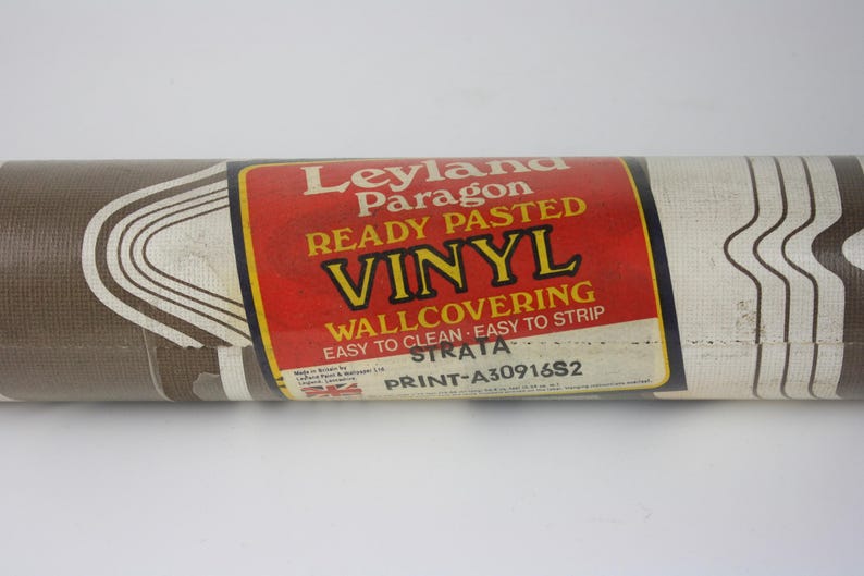 Op de afbeelding: Een rol bruin en wit vinyl behang met een golvend patroon. Het label vermeldt "Leyland Paragon Ready Pasted Vinyl Wallcovering Easy to Clean Easy to Strip Strata Print-A30916S2".