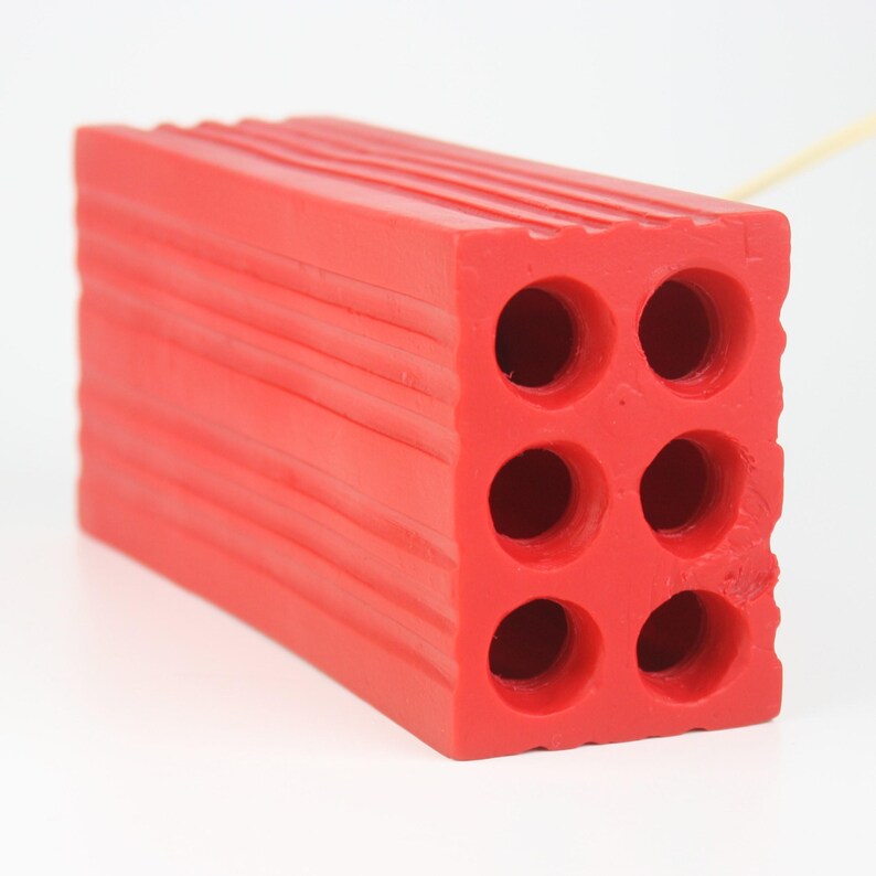 Pu&ograve; includere: Un oggetto rosso vivo a forma di mattone con sei fori circolari e scanalature orizzontali. Il mattone ha una superficie strutturata ed &egrave; realizzato in un materiale solido. Potrebbe essere un giocattolo o un oggetto decorativo.