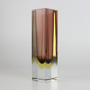 Peut inclure: Un vase en verre rectangulaire avec une base claire et facettée. La partie supérieure présente des panneaux verticaux mauves et jaunes, créant un contraste de couleurs saisissant. Ce vase décoratif est idéal pour exposer des fleurs ou comme pièce d'art à part entière.