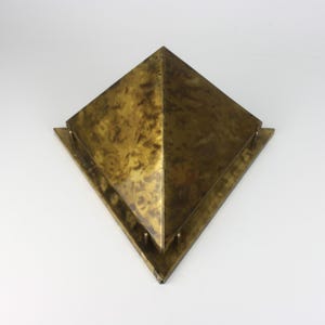 Könnte beinhalten: Vintage Wandleuchte in Pyramidenform aus Messing. Die Leuchte hat eine quadratische Basis mit pyramidenförmiger Spitze. Das Messing hat ein marmoriertes, gealtertes Aussehen. Die Leuchte ist für die Wandmontage konzipiert und eine dekorative Leuchte.