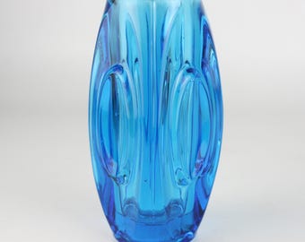 May include: A vibrant, oval-shaped, turquoise-blue glass vase. The vase features a series of vertical, curved indentations that create a textured surface. The design gives the vase a unique, artistic appearance. The vase is suitable for displaying flowers or as a decorative piece.