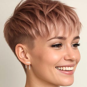 Peut inclure: Une femme avec des cheveux courts, roses clairs et en couches, et une coupe en dessous rasée. Elle porte de petites boucles d'oreilles en forme de barres argentées. La femme sourit, montrant ses dents, et a un eye-liner foncé.