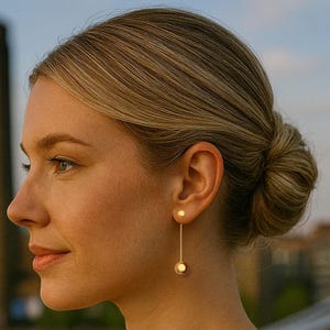 May include: A pair of gold earrings. Each earring has a small, round stud at the earlobe, with a long, thin bar suspending a larger, spherical charm. The earrings are a simple, elegant design.