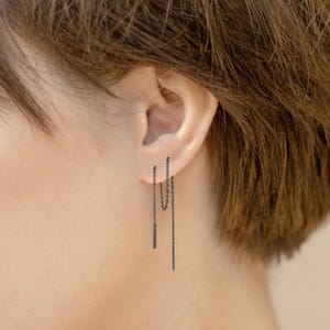 May include: A pair of black chain earrings with a small bar pendant hanging from each chain.