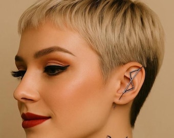 May include: A woman with short blonde hair and dark eyeliner. She is wearing a black ear cuff with a geometric design. The ear cuff is adorned with small, sparkling stones. A tattoo of a plant is visible on her neck.