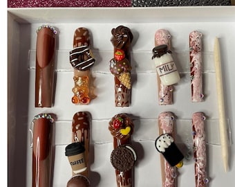 May include: A set of ten long, brown and decorated artificial nails. Designs include a donut, gummy bear, ice cream cone, milk bottle, and coffee cup. Some nails have a glittery accent at the base. A wooden stick is included.