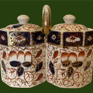 May include: A pair of octagonal porcelain sugar jars with a gold handle. The jars have a white background with red, blue, and gold floral designs.