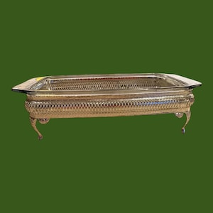 Peut inclure: Un plateau de service rectangulaire argenté avec des détails ornés. Le plateau présente un motif ajouré au centre et est soutenu par quatre pieds incurvés. Les bords sont légèrement surélevés et la surface est réfléchissante.