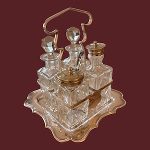 May include: An antique glass and metal condiment set. The set includes four glass bottles with faceted stoppers and a small lidded jar, all on a silver-toned tray. A silver-toned handle arches over the bottles.