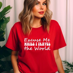 May include: A red t-shirt featuring the white text "Excuse Me While I Travel The World". The shirt has a crew neck and is likely made from a soft fabric. The design suggests a theme of travel and exploration.