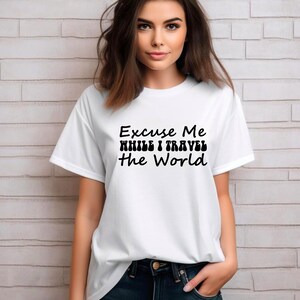 May include: White t-shirt with the text "Excuse Me While I Travel The World" in black. The shirt has short sleeves and a crew neck. The person is wearing dark blue jeans.
