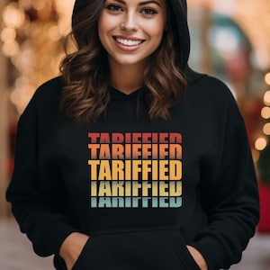 May include: Black hooded sweatshirt with a retro-style graphic design that says "TARIFFED" in a repeating pattern. The graphic is in shades of red, orange, yellow, and blue.