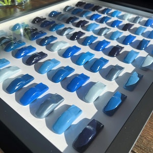 May include: A framed display of small, blue car models arranged in rows, showcasing a gradient of blue shades from dark to light.