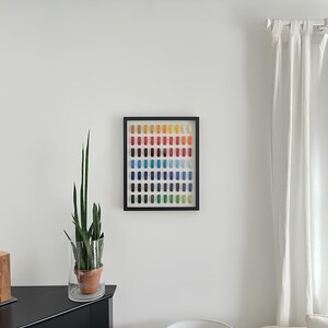 K&ouml;nnte beinhalten: Ein gerahmtes Kunstwerk mit einem Raster aus farbigen Rechtecken in einem Spektrum von Gelb bis Blau. Das Kunstwerk h&auml;ngt an einer wei&szlig;en Wand, mit einer Topfpflanze und einer Lampe im Raum.