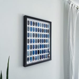 May include: A framed artwork featuring a grid of small blue squares, arranged in a gradient pattern from dark to light blue.