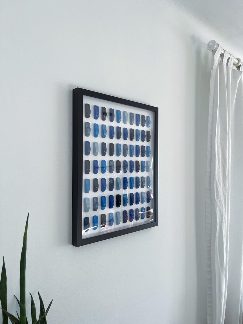 May include: A framed artwork featuring a grid of small blue squares, arranged in a gradient pattern from dark to light blue.