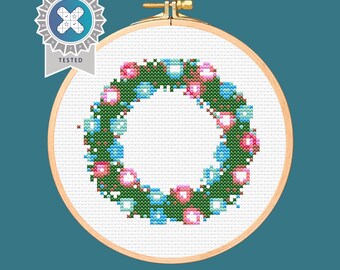 May include: A green wreath with pink and blue baubles. The wreath is in a wooden embroidery hoop.