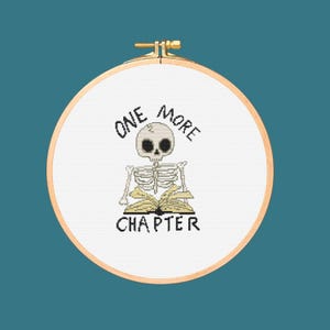 Peut inclure: Un cerceau de broderie blanc avec un motif de point de croix représentant un squelette lisant un livre. Le texte dit "ONE MORE CHAPTER".