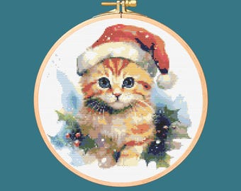 May include: A cute orange tabby kitten wearing a red Santa hat and holding a sprig of holly. The kitten is surrounded by a white snowy background.