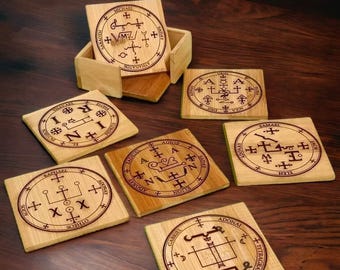 Puede incluir: Conjunto de siete posavasos de madera con grabados de sellos y nombres. Los posavasos son de forma cuadrada y de color marrón claro. Los sellos son de color marrón oscuro y están rodeados por un círculo. Los nombres están escritos en marrón oscuro alrededor de los sellos. Los posavasos están dispuestos en círculo sobre una superficie de madera.
