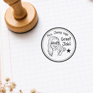 K&ouml;nnte beinhalten: Runder Holzstempel mit einem Cartoon einer Frau mit Brille und dem Text "Mrs. Jenny says Great Job!". Der Stempel ist schwarz-wei&szlig; und hat einen gepunkteten Rand.