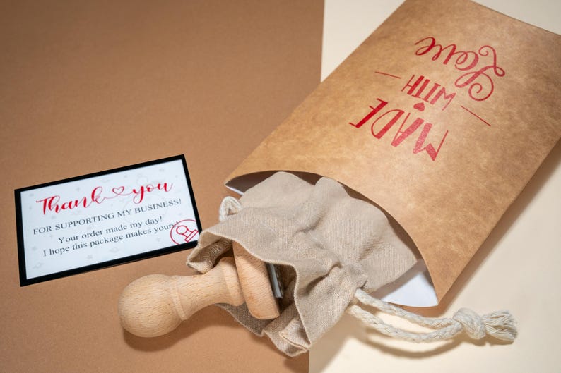 May include: A package with a wooden stamp, a small drawstring bag, and a thank you card. The brown paper bag is printed with "MADE WITH LOVE" in red. The thank you card reads "Thank you for supporting my business!"