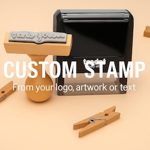 May include: A wooden handle rubber stamp with the text "thanks you" on the rubber die, positioned next to a black self-inking Trodat stamp. The scene includes several small wooden clothespins scattered around the two stamp devices.
