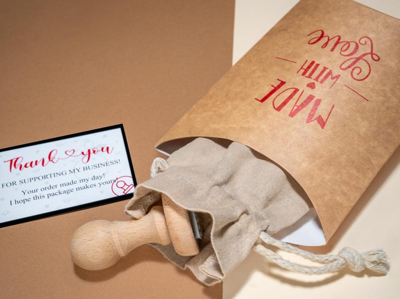 K&ouml;nnte beinhalten: Eine braune Papiert&uuml;te mit den roten Aufdruck "MADE WITH LOVE". Im Inneren befindet sich ein kleiner Kordelzugbeutel mit Holzstempeln. Eine Karte mit den Worten "Thank you" ist ebenfalls sichtbar.