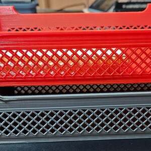May include: Two plastic storage crates stacked on top of each other. The top crate is red and the bottom crate is gray. Both crates have a diamond-shaped grid pattern.