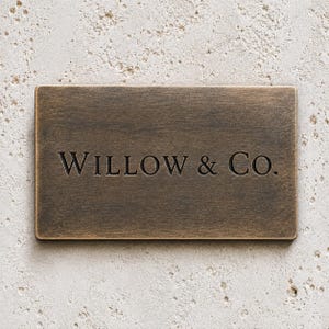 May include: A rectangular bronze-toned metal plaque with a brushed finish. The text WILLOW & CO. is engraved in a dark, serif font across the center of the plaque, which features rounded corners and a flat, smooth surface texture.