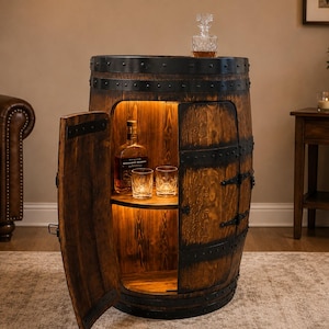 May include: A rustic wooden barrel cabinet featuring a hinged door, internal LED lighting, and a single shelf. The exterior is constructed from dark stained wood planks with black metal bands and hardware. Inside, a glass bottle and two glasses sit.