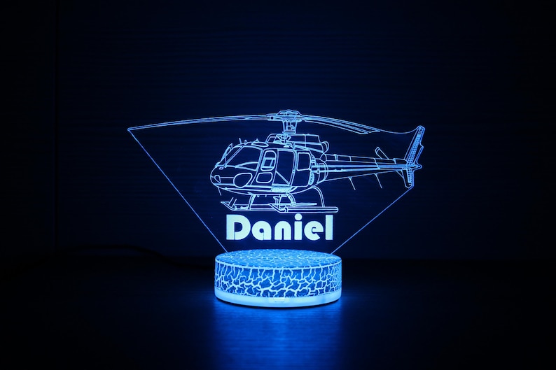 May include: A blue 3D printed night light shaped like a helicopter with the name "Daniel" underneath. The light is on a white base with a textured surface.