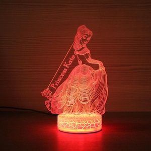 Puede incluir: Luz nocturna LED roja con una silueta de princesa con un vestido fluido y el texto "Princess Kate".