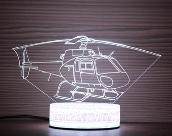 May include: A white LED night light shaped like a helicopter. The helicopter is outlined in white and is sitting on a white base.