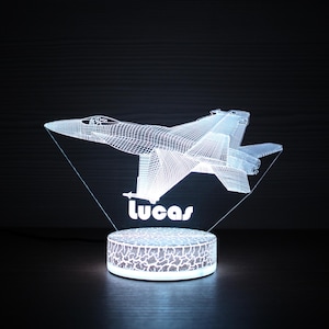 May include: A white 3D printed night light shaped like a fighter jet with the name "Lucas" printed below. The night light is on a white base with a textured surface.