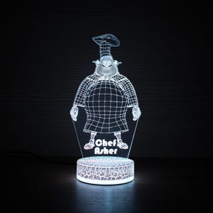 May include: A white 3D printed night light shaped like a cartoon chef wearing a chef's hat. The chef is wearing a white chef's coat and has a large smile. The night light is on a white base with the text "Chef Asher" printed on it.