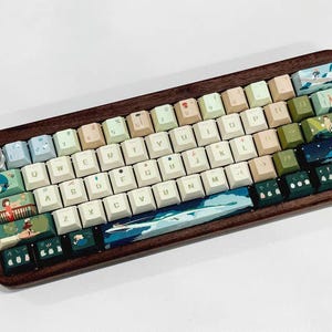 K&ouml;nnte beinhalten: Eine benutzerdefinierte Tastatur mit einem Holzrahmen und einer Vielzahl von Tastenkappen mit verschiedenen Farben und Designs. Die Tastenkappen haben ein hellblaues, gr&uuml;nes und wei&szlig;es Farbschema mit Illustrationen von Blumen, B&auml;umen und anderen naturinspirierten Elementen. Die Tastatur hat auch eine benutzerdefinierte Leertaste mit einem blauen und gr&uuml;nen Design.