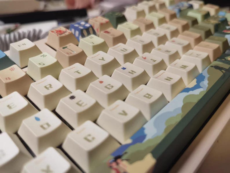 K&ouml;nnte beinhalten: Eine wei&szlig;e mechanische Tastatur mit einem gr&uuml;nen, blauen und braunen Tarnmuster am oberen Rand. Die Tasten haben eine cremefarbene Farbe und zeigen verschiedene Symbole und Buchstaben.
