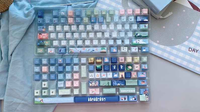 May include: A custom keyboard with a blue and white color scheme. The keys have different designs, including a blue and white striped design, a floral design, and a design with a cat on it. The keyboard also has a blue space bar with the word "TokoToko" printed on it.