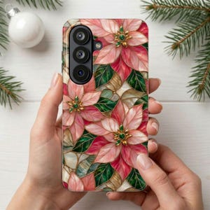 May include: A smartphone case featuring a stained-glass style pattern of pink poinsettia flowers with green leaves and gold-toned centers. The design covers the back of the device, including the camera module area, with a repeating floral motif.