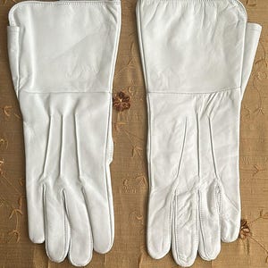 May include: A pair of white leather gloves with a stitched design. The gloves are made of a soft, supple leather and have a classic look.