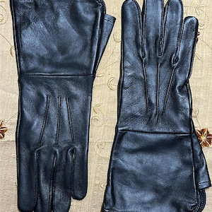 May include: A pair of black leather gloves with long gauntlets. The gloves are made of smooth leather and have visible stitching along the seams. The gloves are designed to cover the hands and wrists.