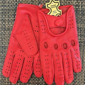May include: A pair of red leather driving gloves with perforated detailing and a button closure. The gloves have the text "Genuine Leather" and "Echt Leder" on a yellow tag.