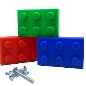 May include: Three brightly coloured toy building blocks in green, red, and blue are stacked. Each block has six circular studs. Several silver screws are in front of the blocks.