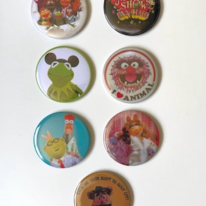 Op de afbeelding: Zeven ronde buttons met Muppets-personages. De ontwerpen bevatten een groepsfoto, het logo van The Muppet Show Fan Club, Kermit de Kikker, Animal met de tekst I Love Animal, Dr. Bunsen Honeydew en Beaker, Miss Piggy en Fozzie Bear met de tekst Exercise Your Right To Goof Off.
