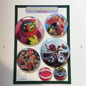 Op de afbeelding: Een set van vijf ronde buttons met de personages van The Electric Mayhem uit The Muppets, gepresenteerd op een rechthoekige kaart met de tekst Electric Mayhem Button Pack en het Eden-logo onderaan.