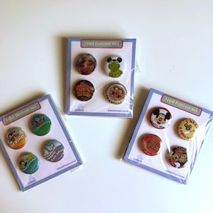 May include: Three sets of four round pin-back buttons packaged on white cards labeled Mini Button Set. The buttons feature various colorful cartoon character graphics and text including 1st Visit, Happily Ever After, Happy Birthday, The Muppet Show, Animal, Mickey Mouse, and I Like Disneyland.