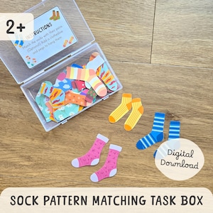 May include: A clear plastic box filled with colorful sock cutouts, with pairs of socks scattered around. The socks feature various patterns and colors, including stripes, polka dots, and floral designs. The text "SOCK PATTERN MATCHING TASK BOX" is at the bottom.